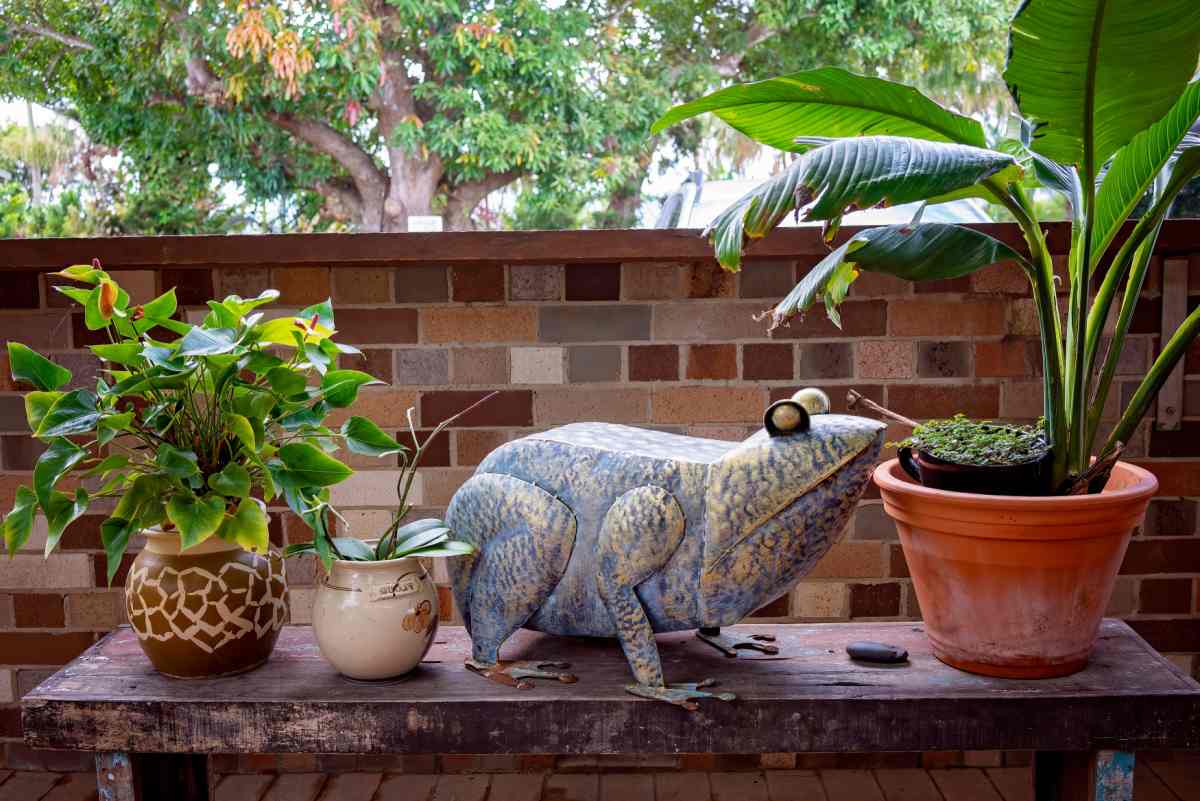 Large metal frog yard art near some plants on a patio.