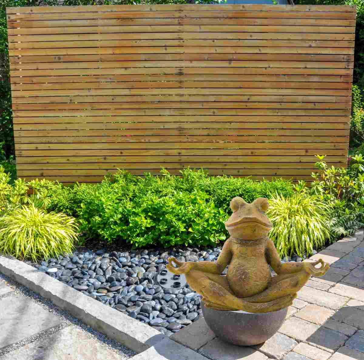 Frog meditation statue in a garden with a hanging screen.