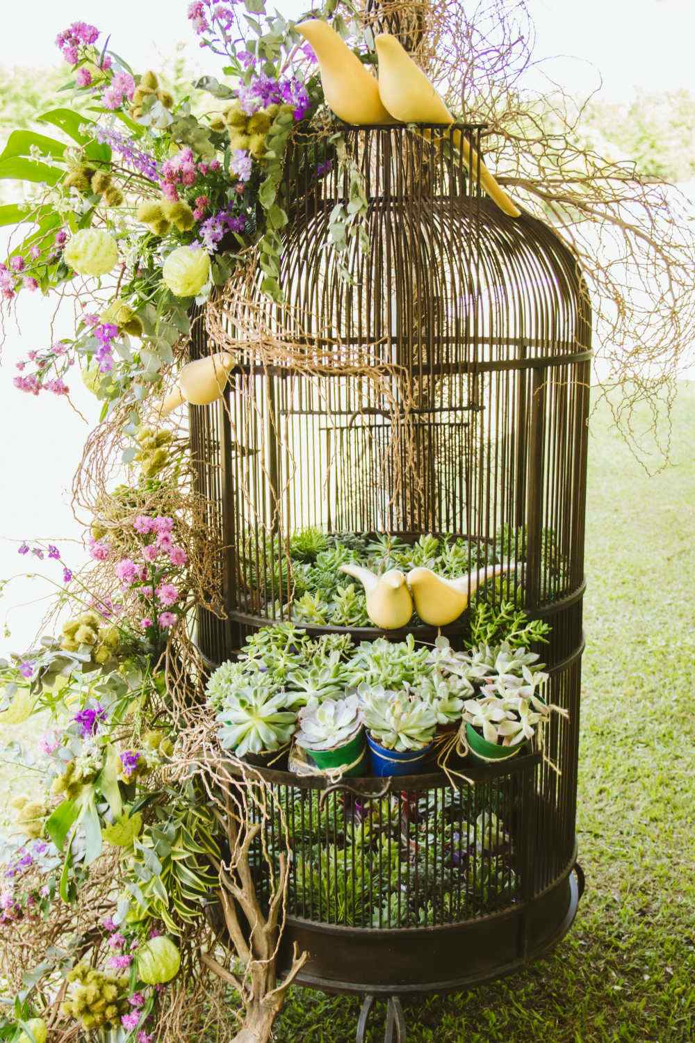 Elaborate arrangement in a bird cage with birds, succulents and silk leaves and flowers.