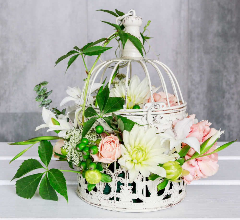 Pretty white bird cage with silk flowers and leaves.