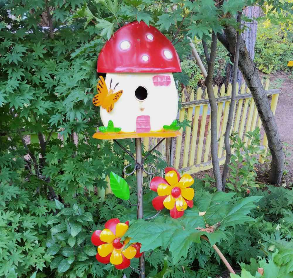 Whimsical birdhouse made of metal in a garden setting.