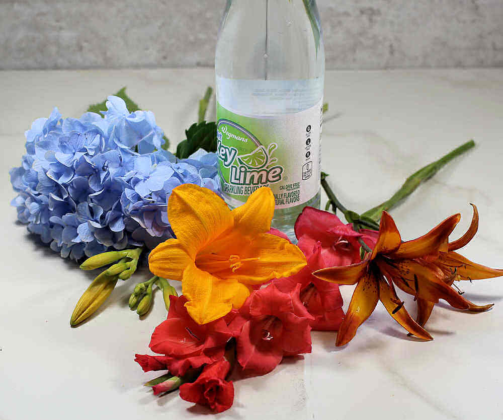 Bottle of key lime soda with lilies, gladioli and hydrangea.